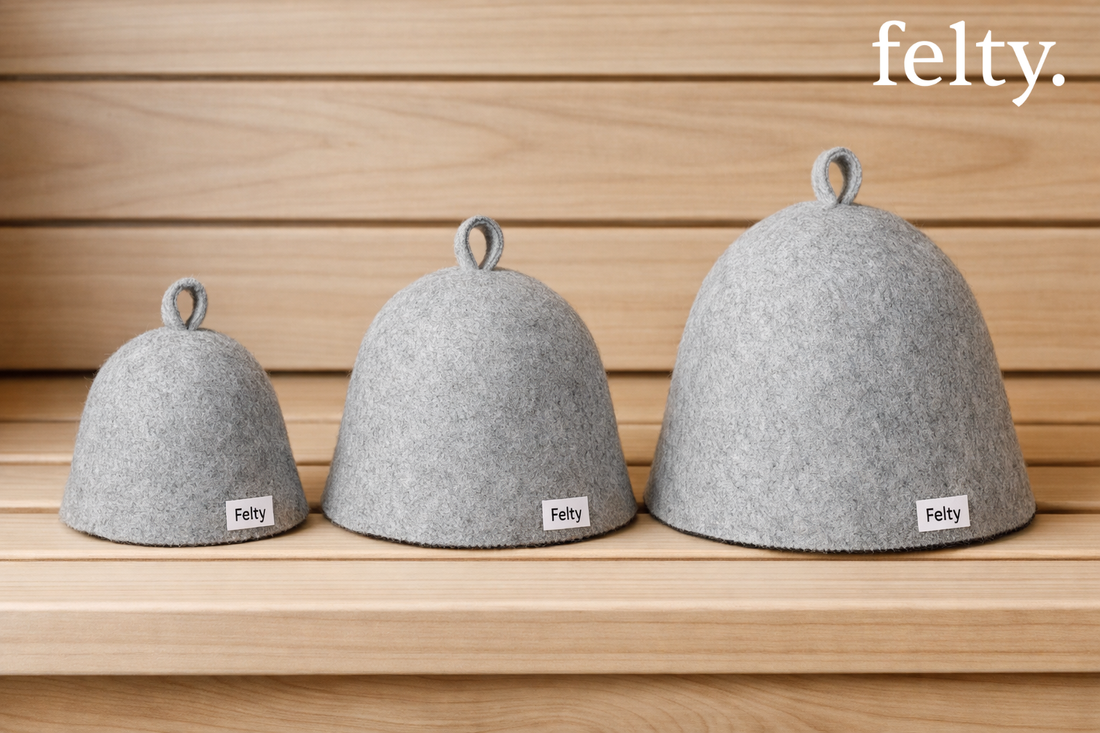 Three light grey wool sauna hats in small, medium, and large sizes arranged on a wooden sauna bench.