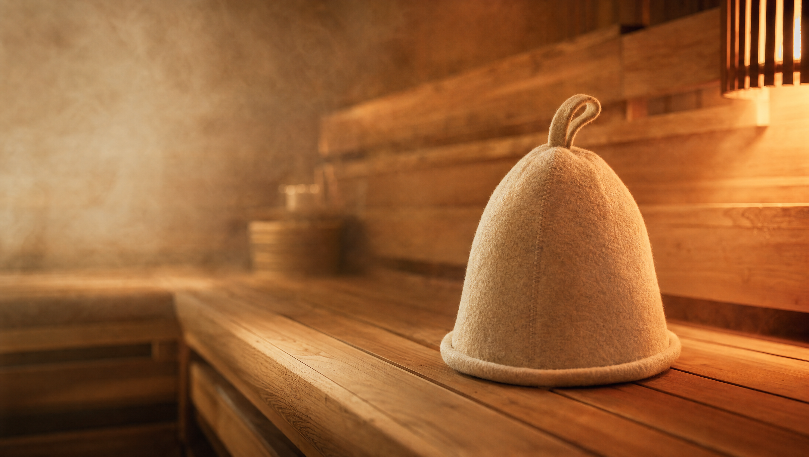 Person sitting comfortably in a hot, steamy sauna while wearing an ivory wool sauna hat that works to prevent head overheating