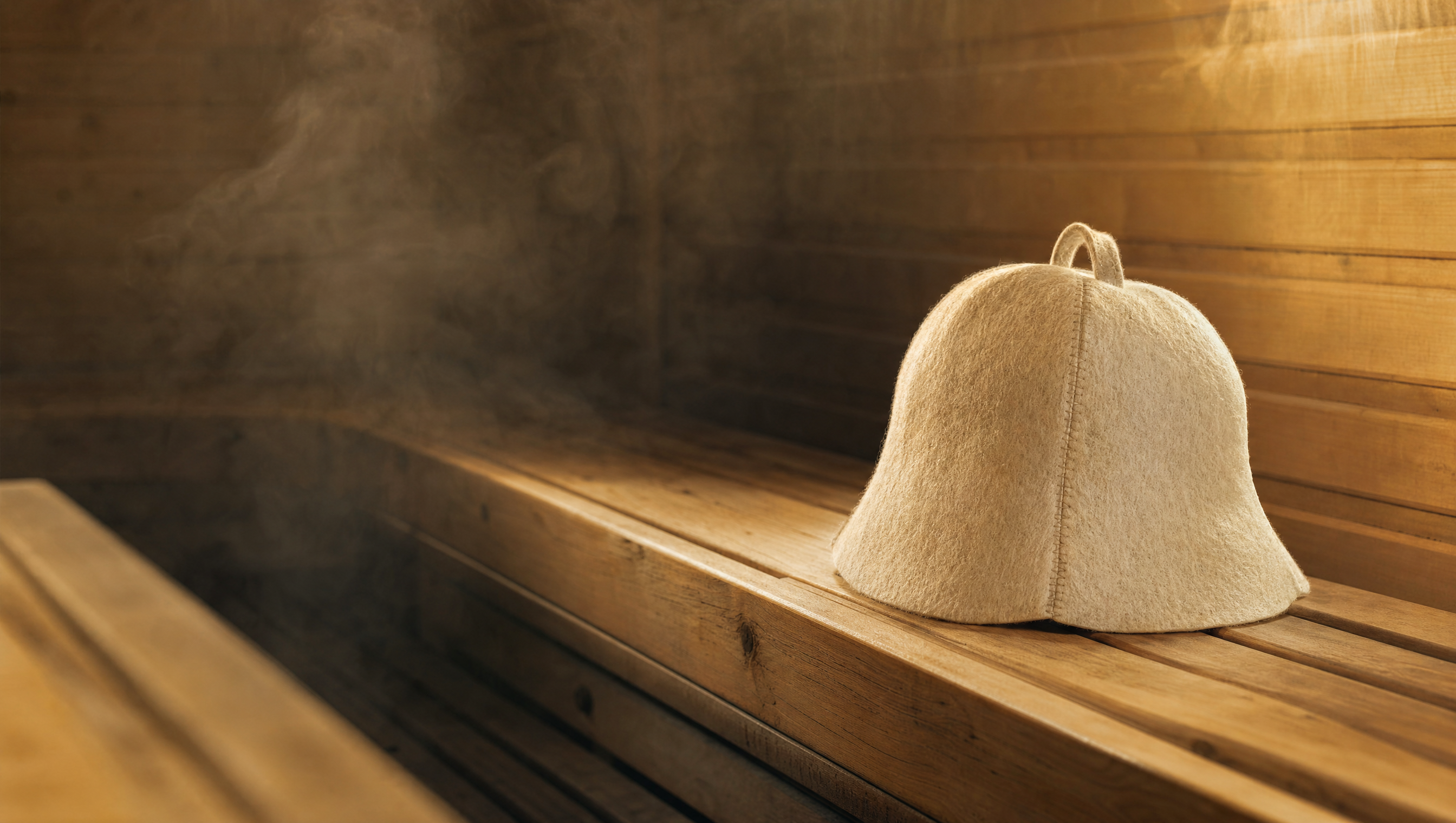 Person relaxing on a sauna bench wearing an ivory wool sauna hat, illustrating why wear a sauna hat in high heat
